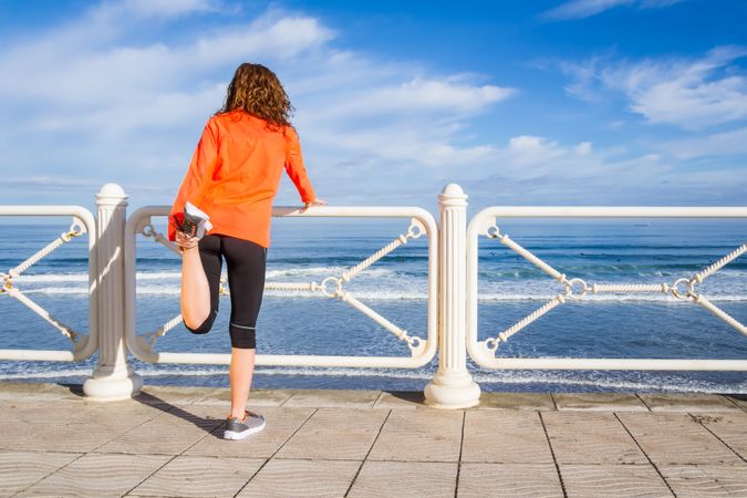Back of woman stretching legs before running on the beach promenade on a summer morning