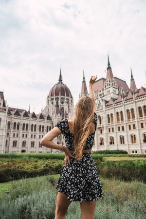 Long haired woman raising hand to ancient old building