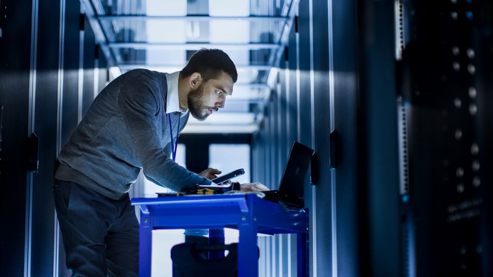 IT Engineer with Tool Cart Stands at a Corridor of a Large Data Center Full of Rack Servers