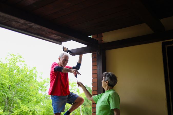 Woman giving a screwdriver to her husband while he is installing the new light on their home.