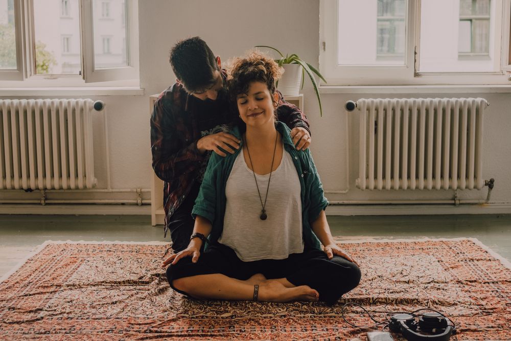 Man rubbing shoulders of joyful woman resting on floor at home