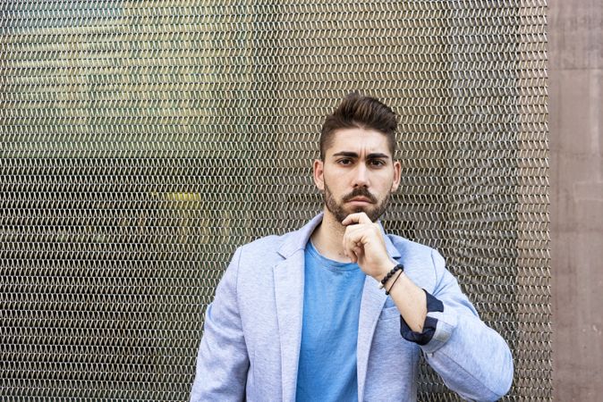 Portrait of young bearded man leaning on wired wall and looking at camera