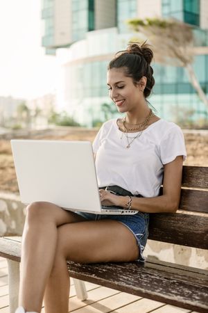 Woman sitting on bench working on her laptop