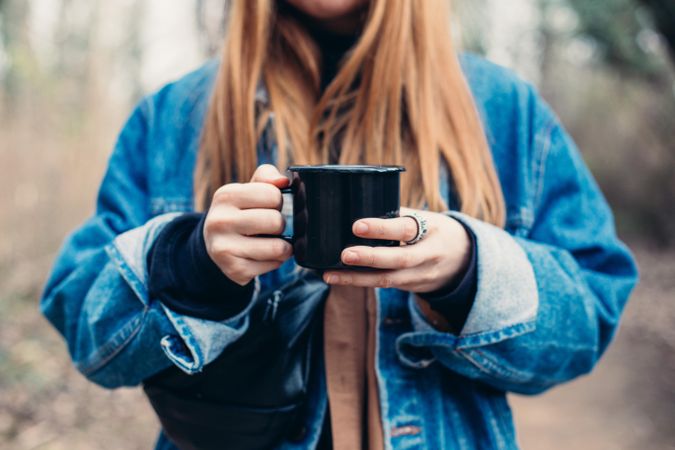 Woman holding a warm mug of coffee in the forest