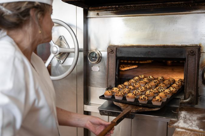 Unrecognizable baker woman taking out a cupcake tray from a stone oven