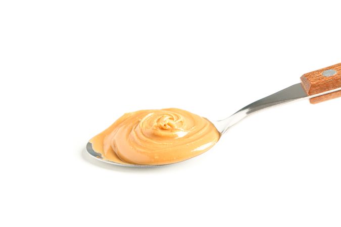 Creamy peanut butter in spoon isolated on light background, closeup. A traditional product of American cuisine