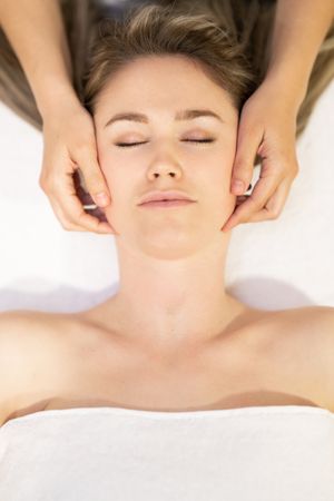 Young woman with masseuse working on her jaw in a spa