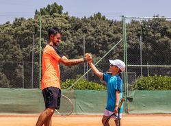 Father and son playing tennis together on a dirt court
