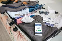 Businessman suitcase prepared for business trip with covid passport on mobile