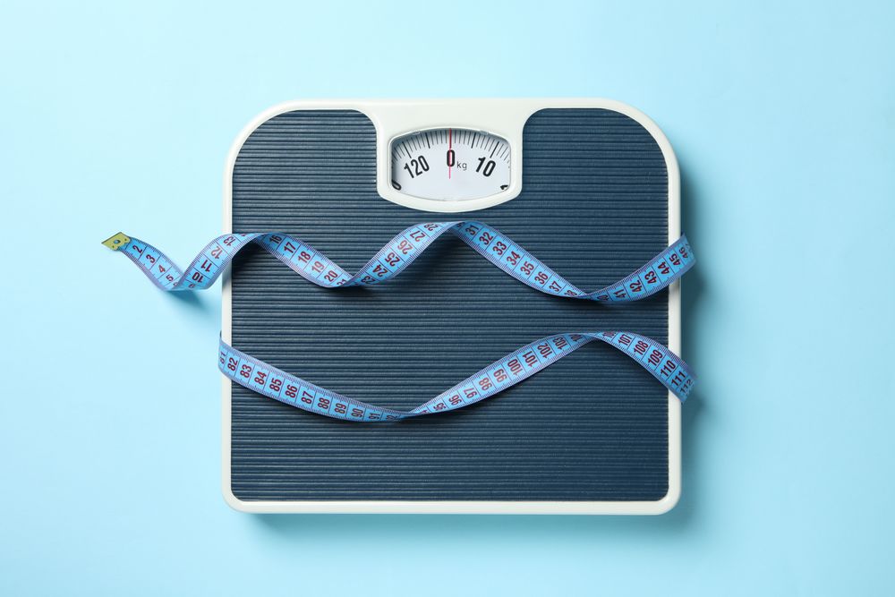 Scales and measuring tape on blue background. Weight loss concept