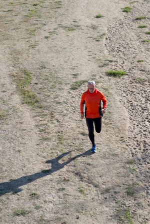 Looking down at fit man running on sandy ground