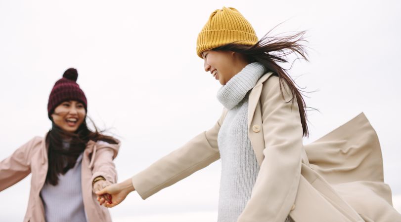 Two young women in winter clothes having fun and holding hands