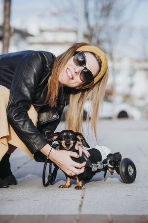 Smiling woman near dog with wheelchair on street