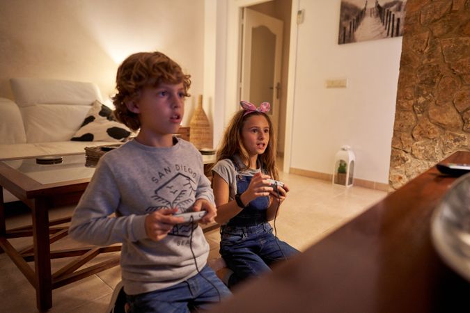 Exited children sitting on knees and playing game with joystick