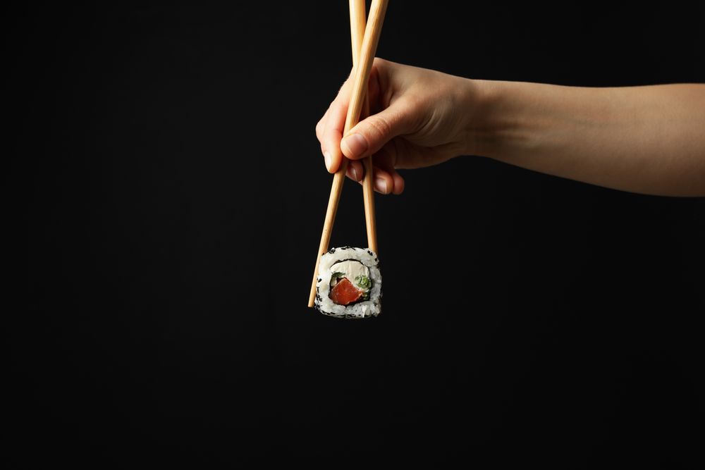 Female hand with chopsticks hold sushi roll on dark background. Japanese food
