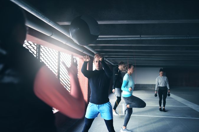 Two men throwing a medicine ball in foreground of a group of people doing circuit training