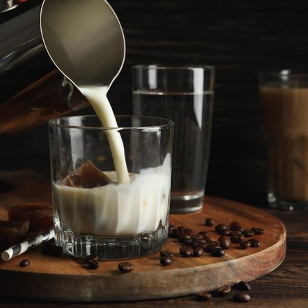 Milk is poured into a glass of coffee. Composition with ice coffee