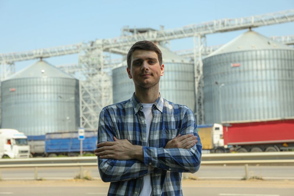 Young man against grain silos. Agriculture business