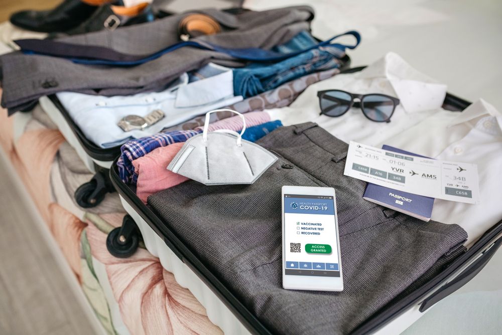 Businessman suitcase prepared for business trip with covid passport on mobile