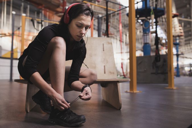 Smiling woman with headphones lacing shoe in gym