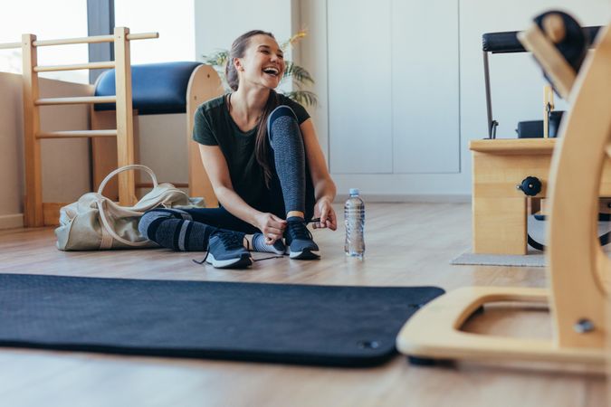 Smiling woman wearing her shoes after workout sitting at the gym