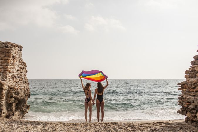 Females standing with rainbow flag on seashore