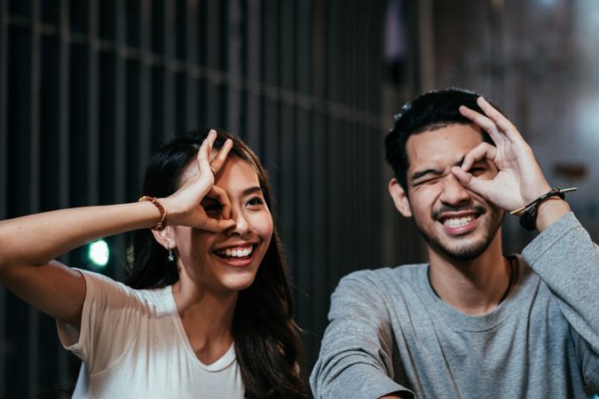 Asian couple circling eye with hand for photo