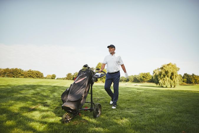 Man pushing golf clubs on course