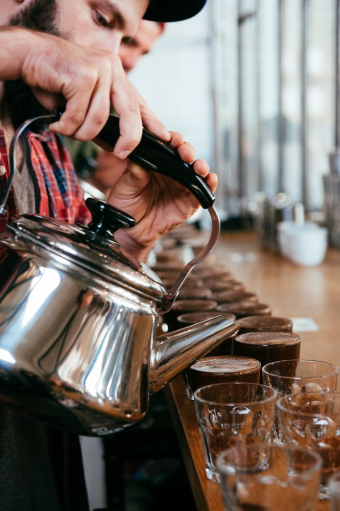 Close up cropped shot of man’s face pouring hot water into glasses for coffee tasting