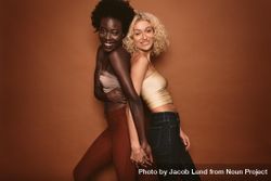 Portrait of two young women standing back to back and looking at camera on brown background 41pMD5