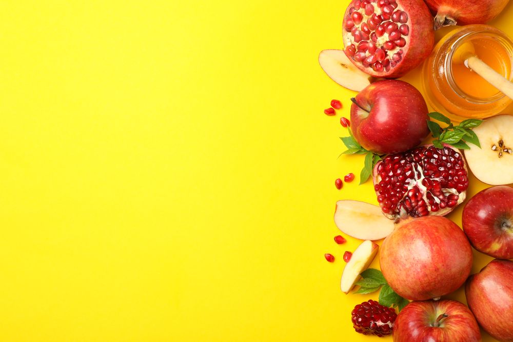 Top view of fresh apples, pomegranate and honey on side of yellow background with copy space