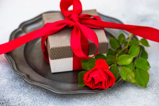 Red ribbon wrapped giftbox on table setting with rose