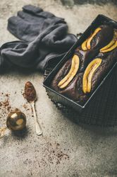 Freshly baked dark chocolate banana bread cake on concrete counter, with cocoa powder