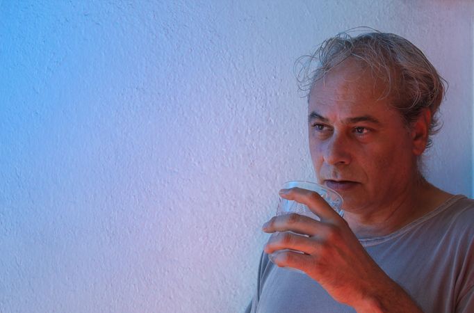Middle aged in gray shirt holding a glass of water looking away