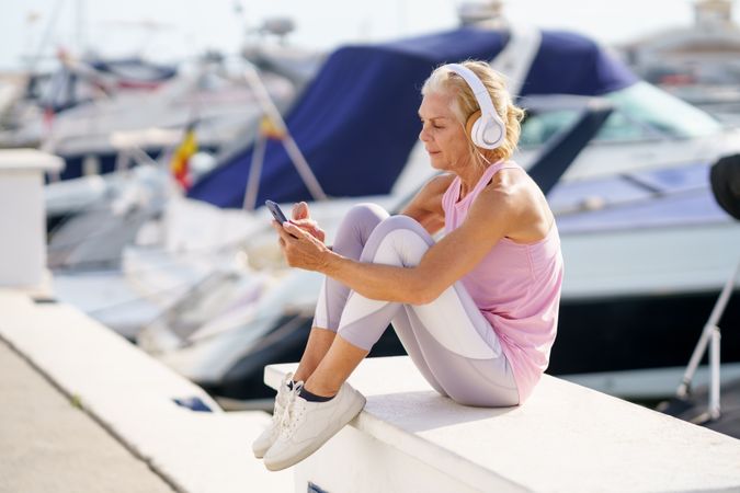 Mature female in fitness clothing texting on waterfront