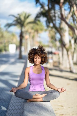 Black woman with afro hairstyle meditating near the beach, vertical