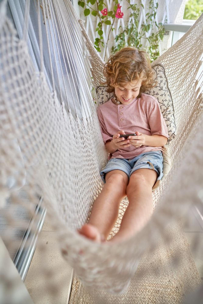 Adorable boy sitting in hammock with smartphone
