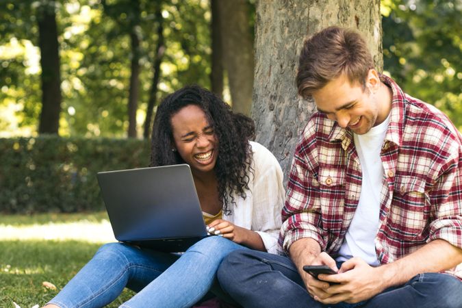 Multiracial couple studying in the park with laptop