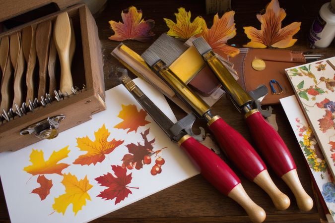 Autumnal leaf painting tools and samples arranged on a dark wood surface