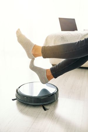 Woman sitting on sofa with robot vacuum cleaner on floor