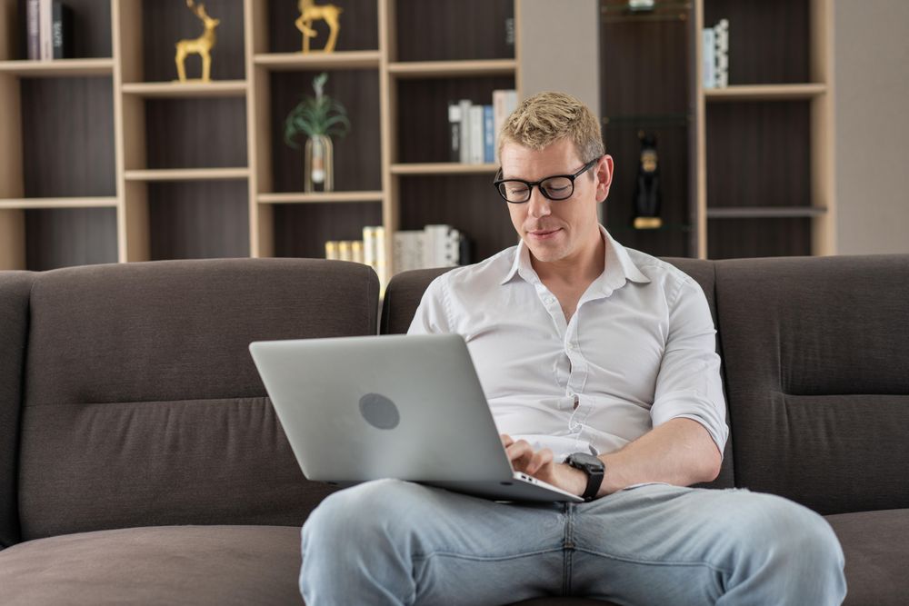 Man working with laptop or watching movie on couch in the living room at home