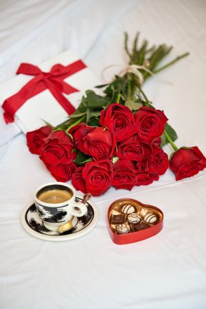 Bouquet of red roses and cup of coffee on bed