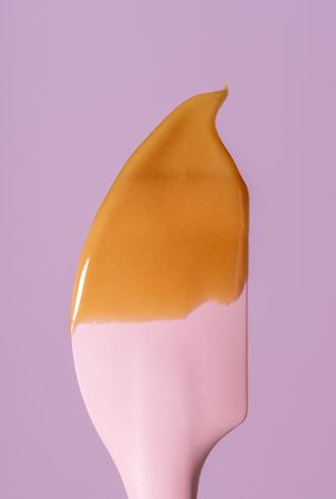 Caramel sauce dripping on a silicon spatula, minimalist on a pink background