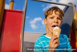 Close up of a boy eating an ice cream sitting on a slide 4AzVR8