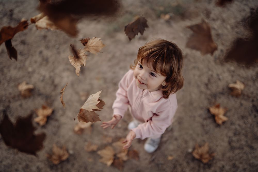 Joyful child scattering leaves on lawn in park