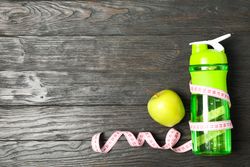 Bottle, measuring tape and apple on wooden background, copy space