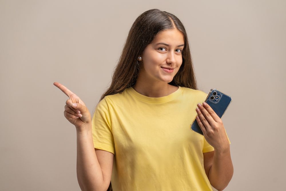 Confident young woman with a phone, pointing and recommending something.