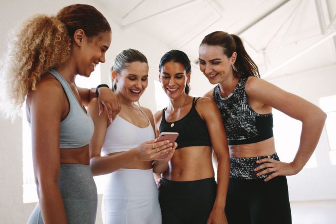 Close up of fit women standing together after workout and looking at a mobile phone