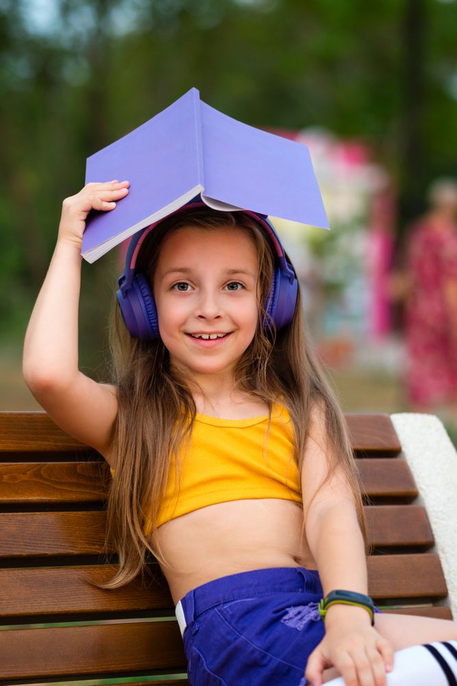 Preteen school girl with book on bench in park
