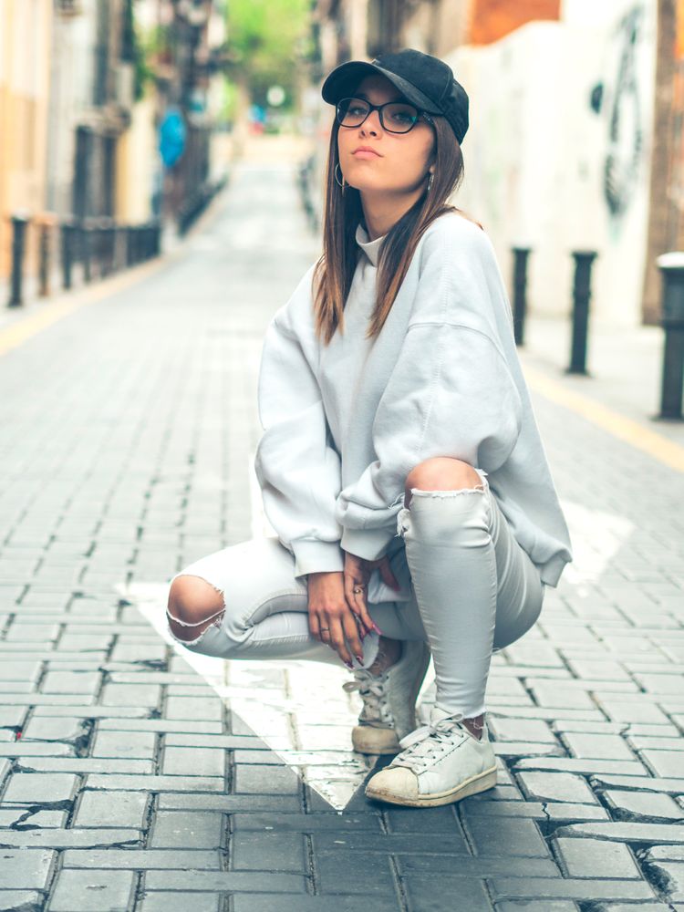 Young trendy woman sitting against street